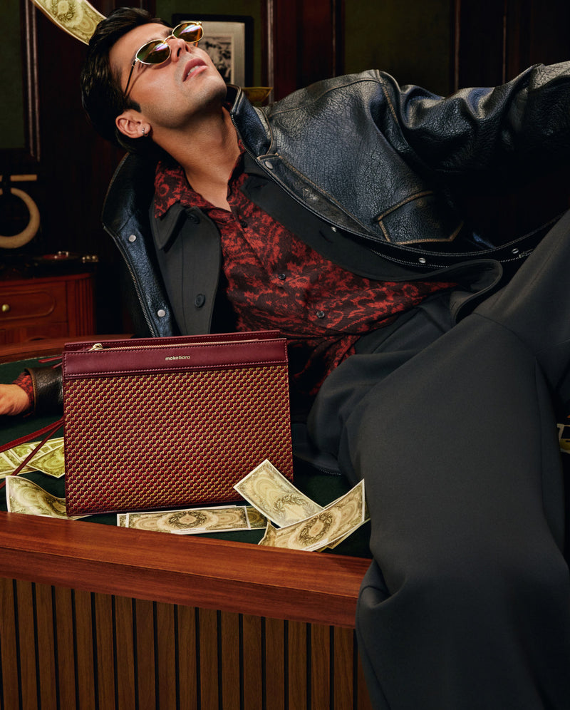 Man lounging at a card table as banknotes fly, maroon Freddie’s Pouch beside him
