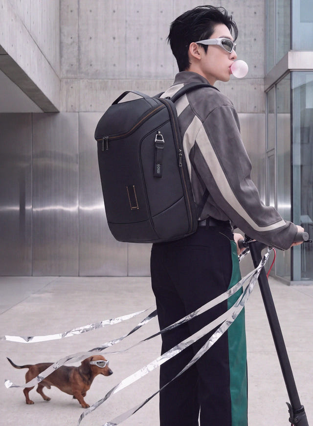 A rider on an e-scooter with a black Transit Z backpack, walking a dachshund